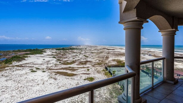 Uitzicht op het strand vanaf een overdekt balkon met zuilen en een glazen balustrade.