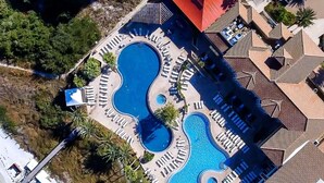 Luchtbeeld van een resort met meerdere zwembaden, ligbedden en een groot gebouw met een rood dak.