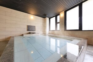 Una amplia piscina interior con agua cristalina, paredes de azulejos y techo de madera.