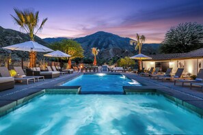 A swimming pool with lounge chairs and umbrellas, surrounded by mountains and trees.