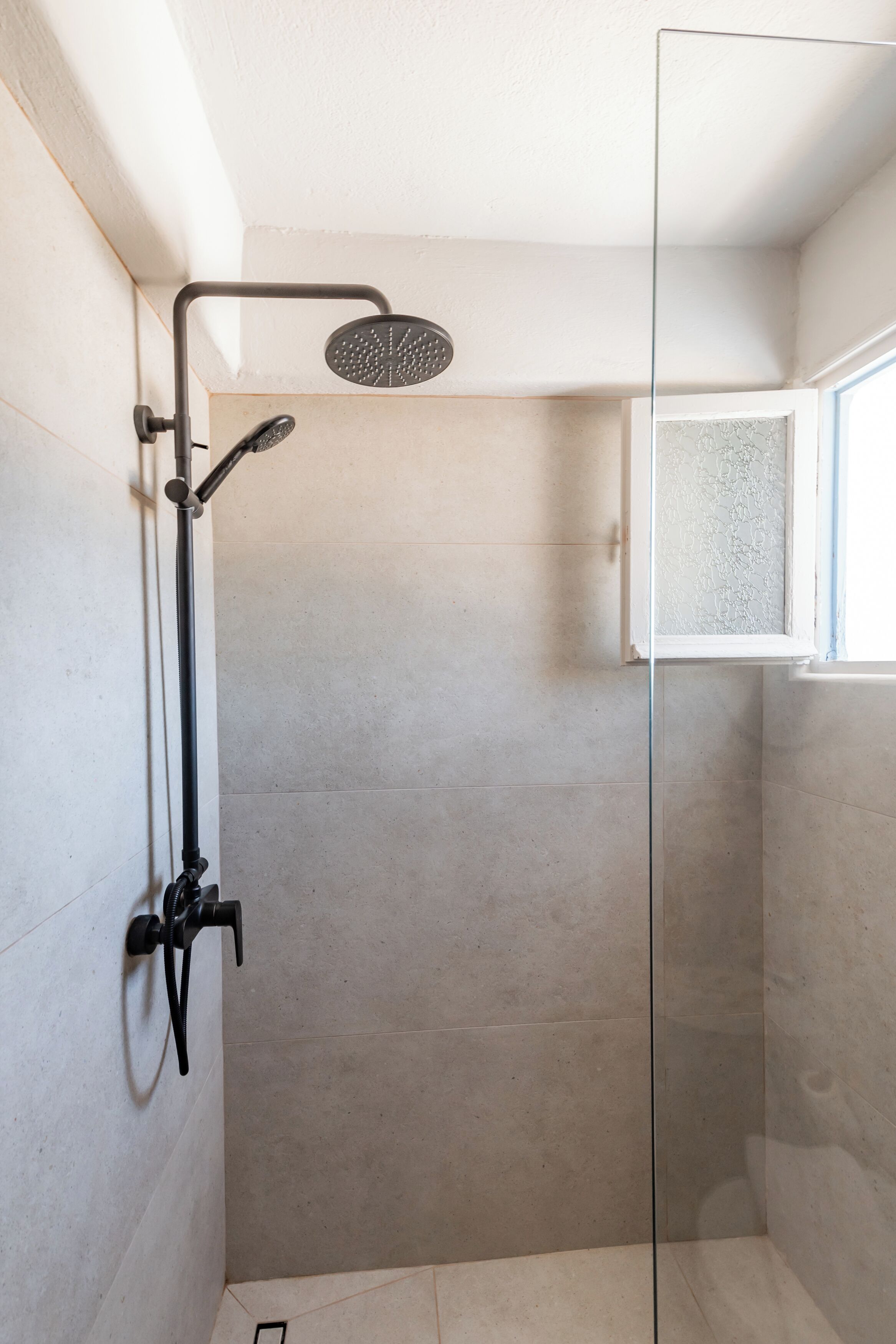 A glass-enclosed shower with a handheld showerhead and a wall-mounted faucet.