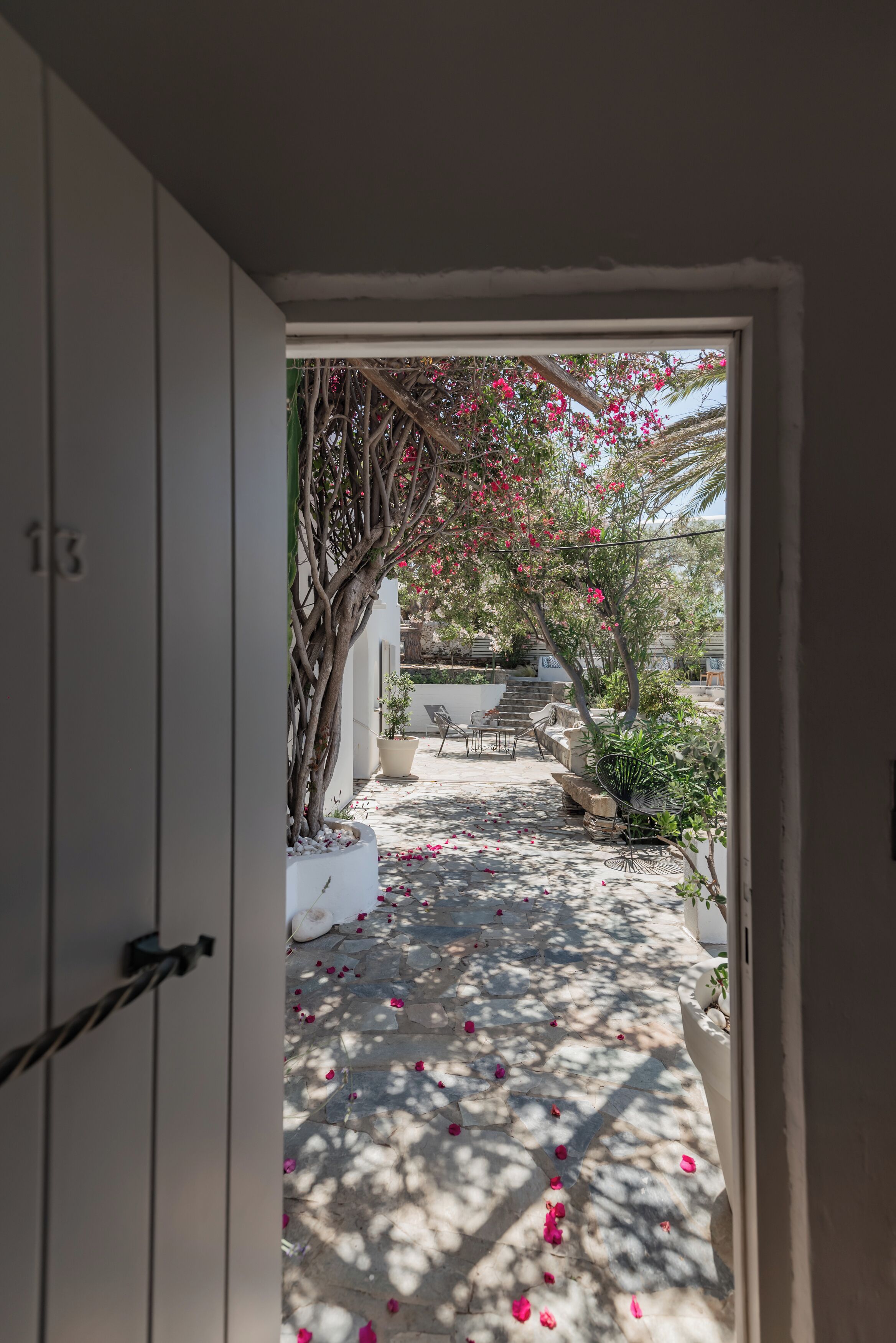 An open doorway leading to a sunlit courtyard with a tree, seating area, and potted plants.