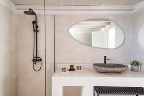 A modern bathroom with a large oval mirror, a vessel sink, and a black showerhead. - Rania Apartments Sea View (Mykonos)