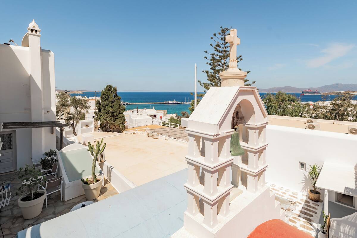 A rooftop terrace with a clear view of the sea, potted plants, and a white architectural structure.