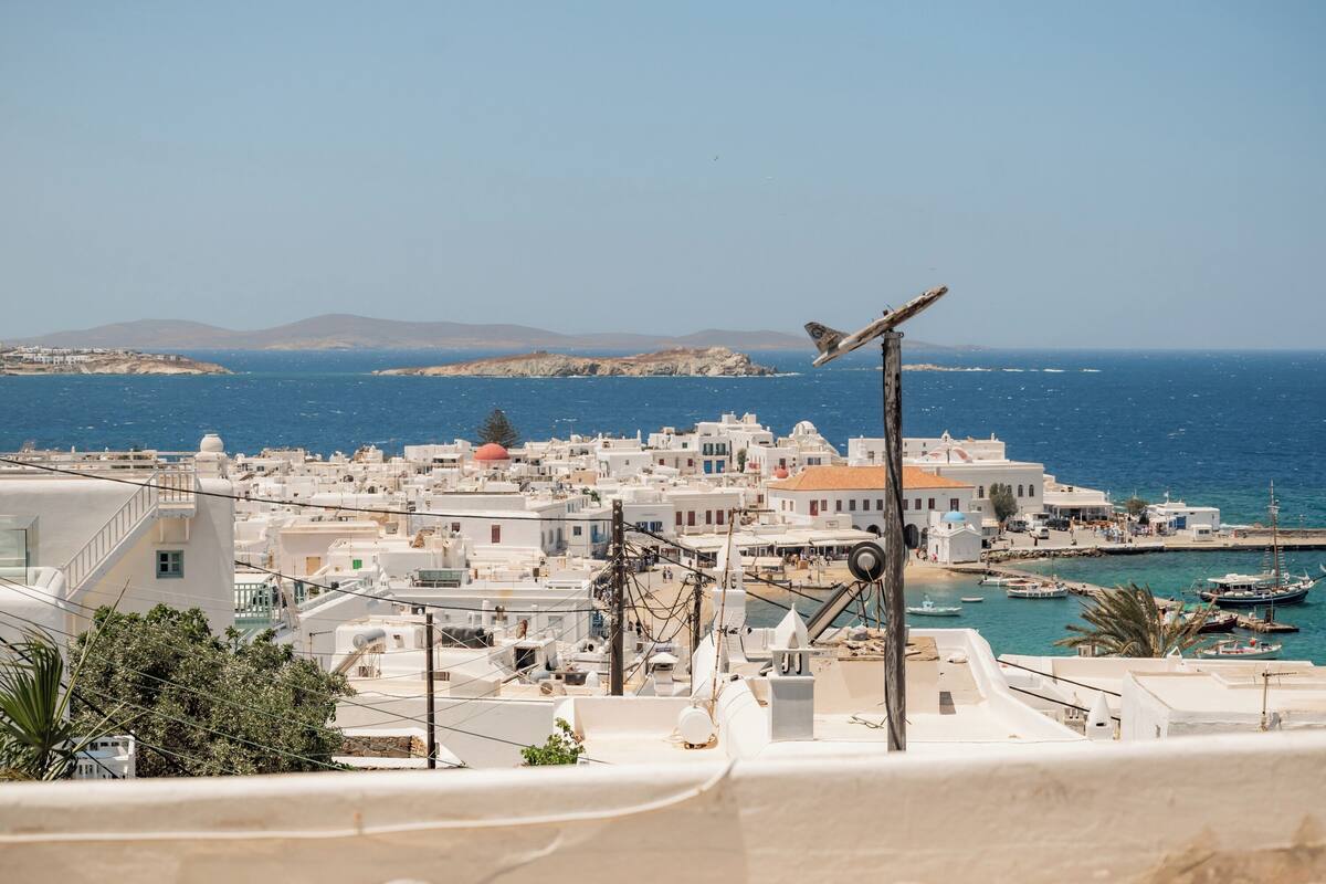 A coastal town with white buildings, a clear blue sea, and a bird on a pole.