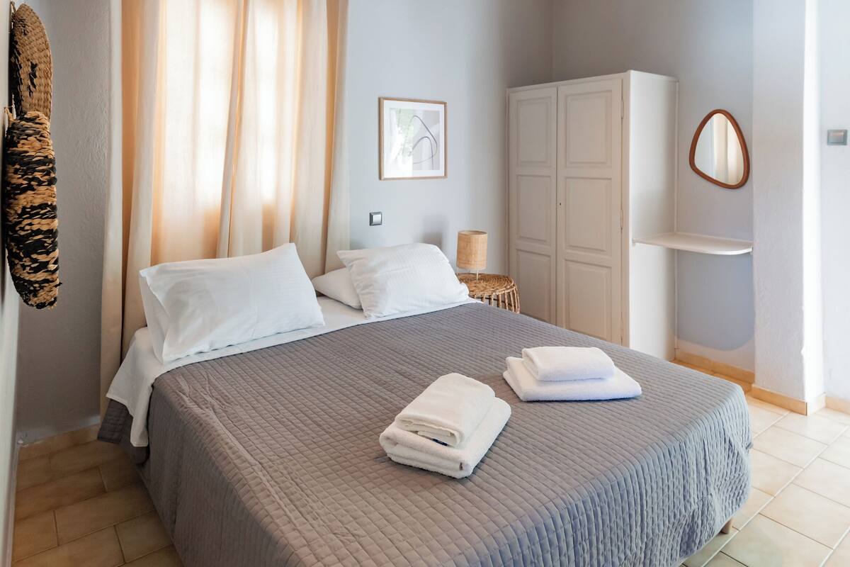 A bedroom with a bed, curtains, a wardrobe, a bedside table, and a wall-mounted mirror.