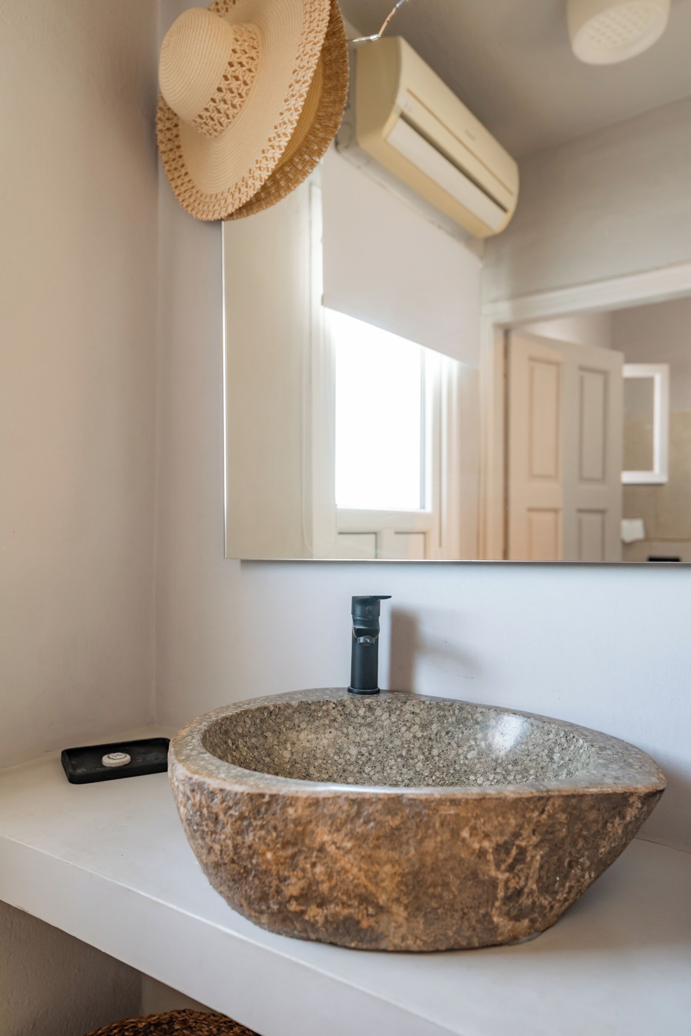 A bathroom with a large stone sink, a mirror, and a straw hat hanging on the wall.