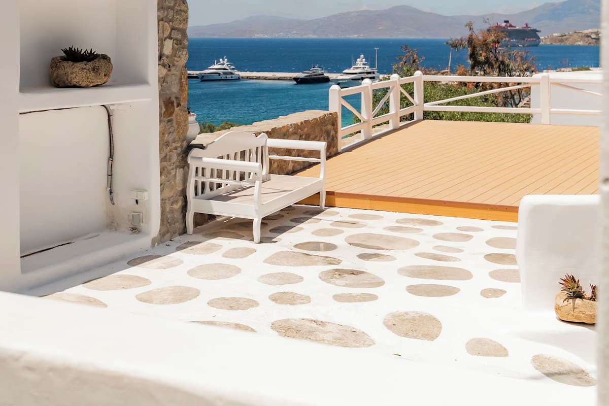 A white balcony with a wooden deck, a white bench, and a small potted plant.