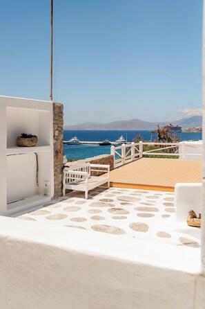 A white balcony with a wooden deck, a white bench, and a small potted plant. - Rania Apartments Sea View (Mykonos)