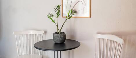 A small room with a round table and two white chairs. There is a framed picture on the wall and a potted plant on the table.