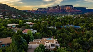A residential area with houses surrounded by dense greenery, a large mountain in the background, and a clear sky. - Sedona Spectacular: Luxury 3BR home with private pool, hot tub, and stunning red rock views. (Sedona)