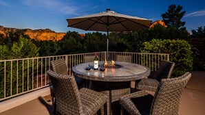 A round outdoor table with wicker chairs, a wine bottle, and glasses, set against a scenic backdrop of mountains and trees. - Sedona Spectacular: Luxury 3BR home with private pool, hot tub, and stunning red rock views. (Sedona)