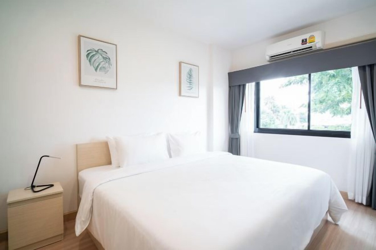 A hotel room with a bed, a nightstand, a wall-mounted air conditioner, and two framed botanical prints.