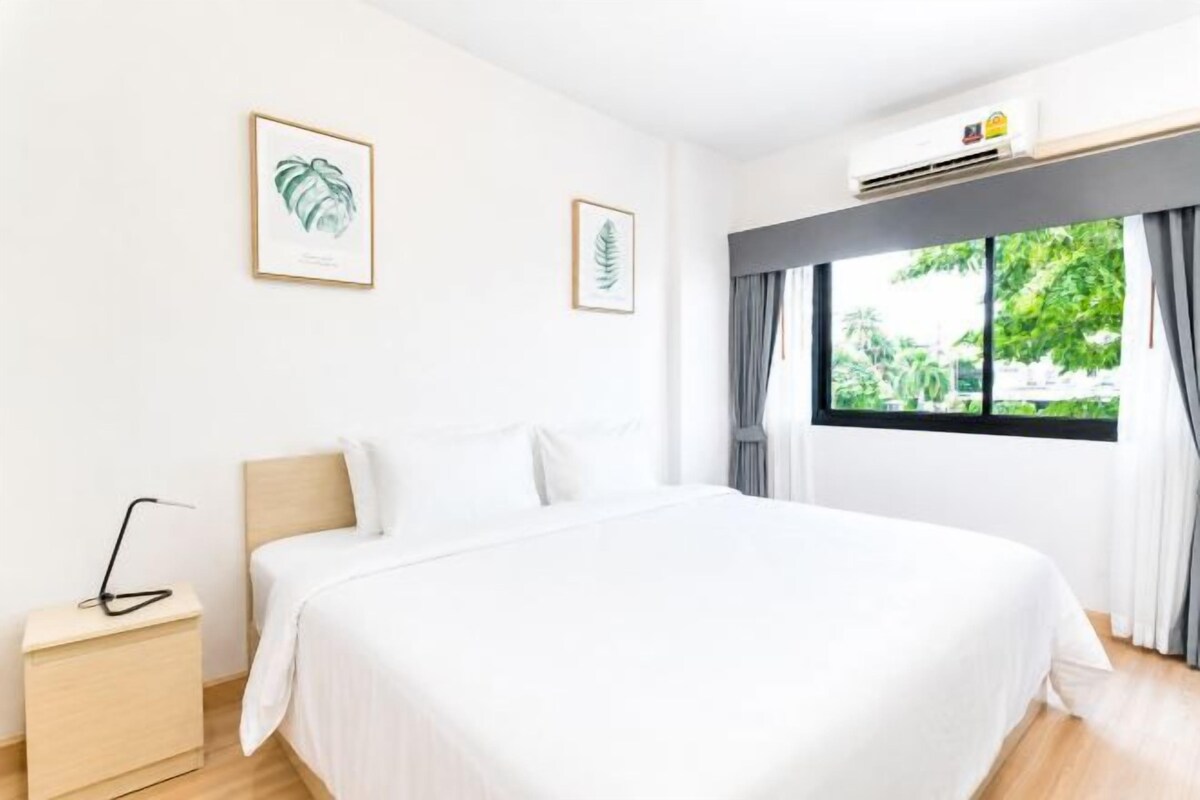 Une chambre d’hôtel avec un grand lit, une table de chevet, une fenêtre avec des rideaux et des œuvres d’art encadrées accrochées au mur.
