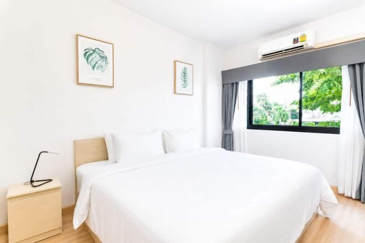 Una habitación de hotel con una cama grande, una mesita de noche, una ventana con cortinas y cuadros decorativos en la pared.