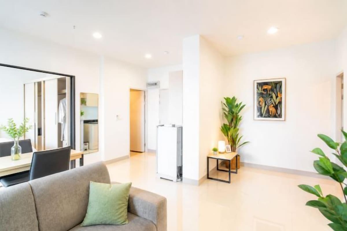 A modern living room with a sofa, a dining table, and a kitchen area in the background.