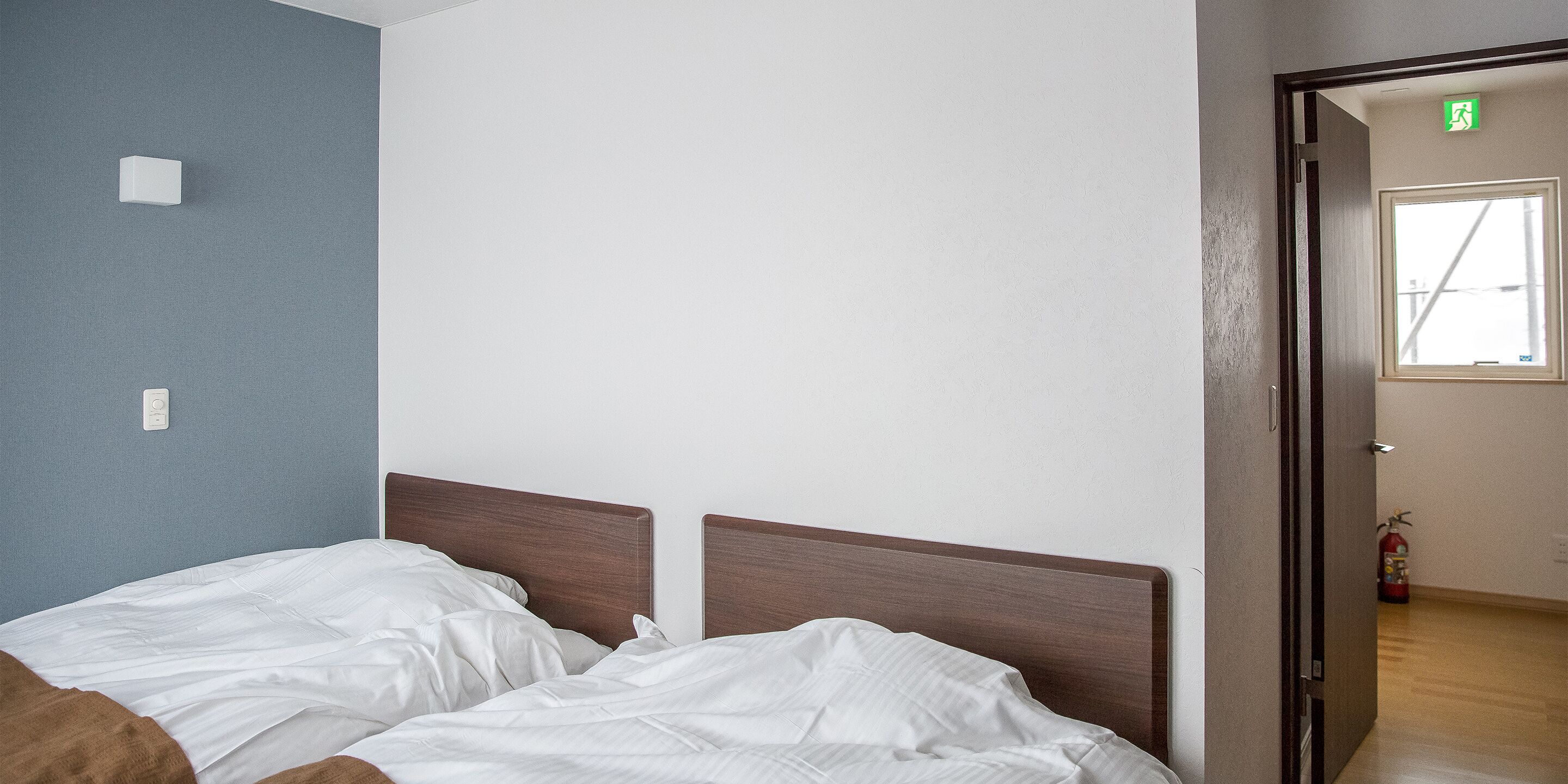 Une chambre à coucher avec une tête de lit en bois, une couvre-lit blanche et un mur d’accent bleu.