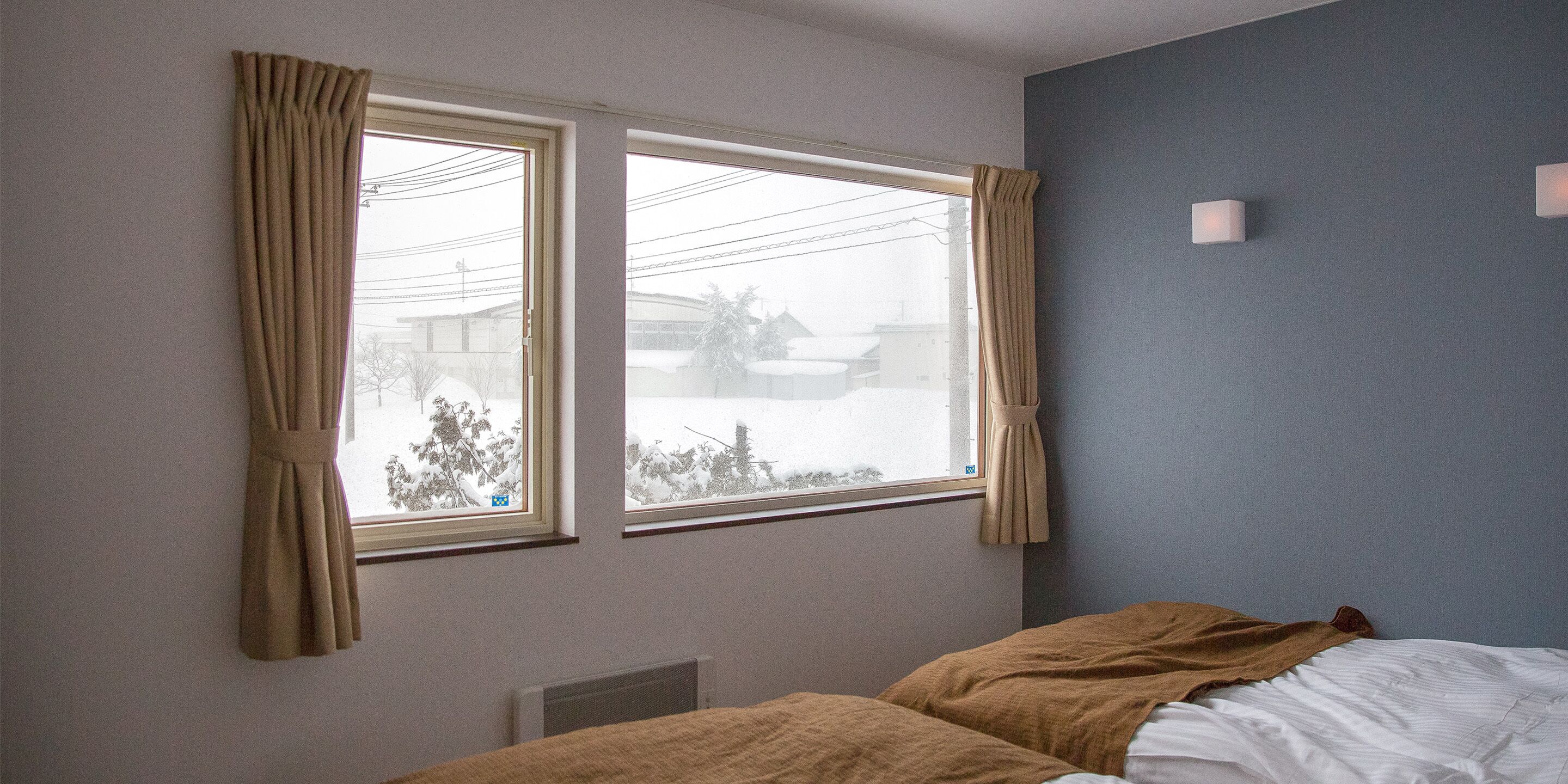 A bedroom with two windows, a bed with a brown blanket, and a blue wall.