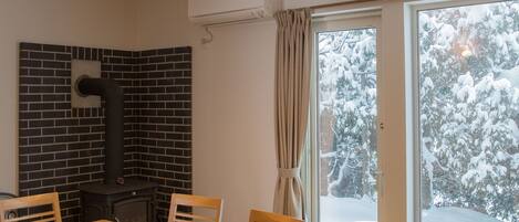 A dining area with a brick wall, a black stove, and a large window with a view of snow-covered trees.