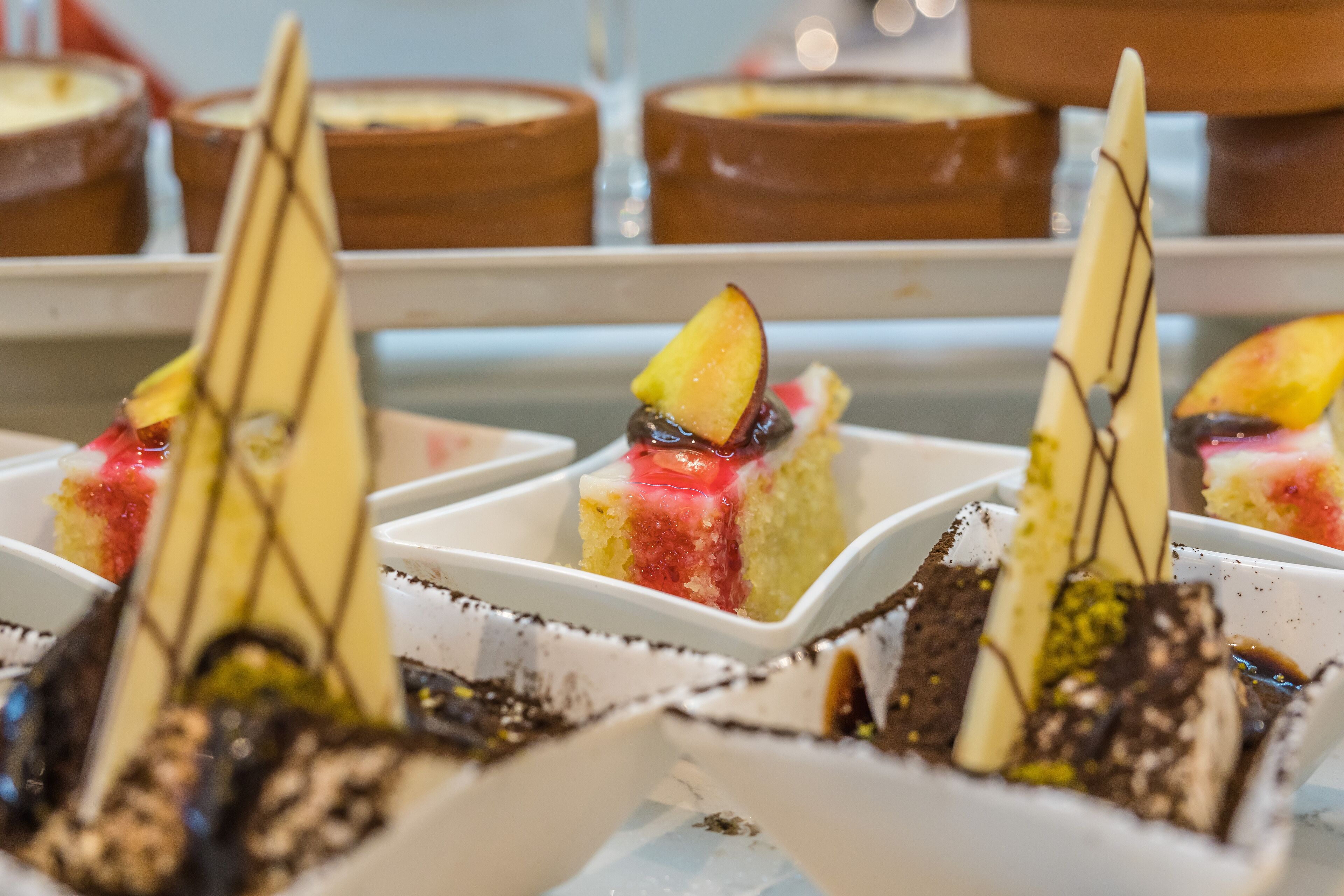 Una presentación de postres con varios pasteles y dulces en recipientes cuadrados blancos.