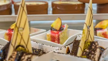 A dessert display with various cakes and pastries in white square dishes.