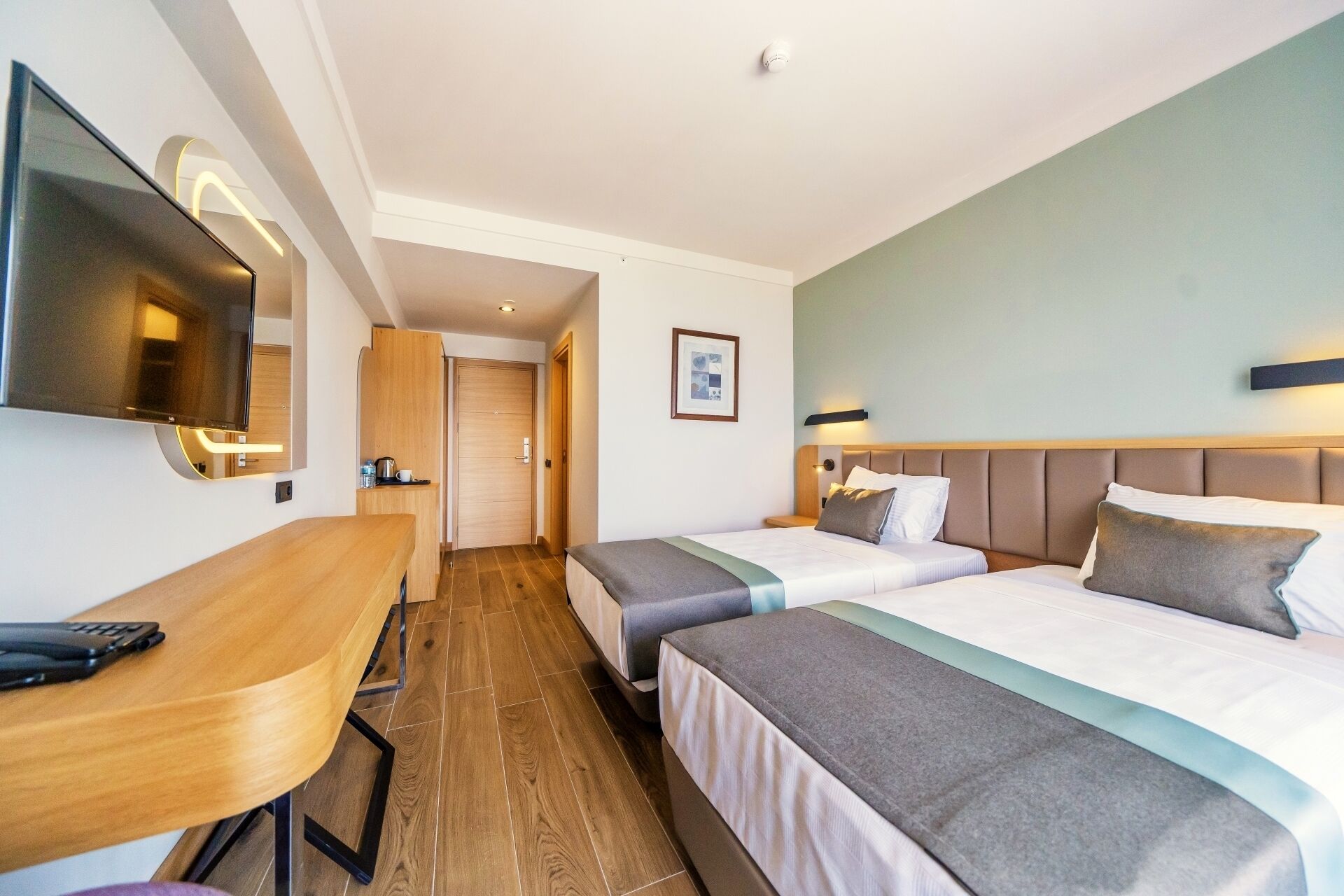A hotel room with two beds, a desk, a flat-screen TV, and a framed picture on the wall.