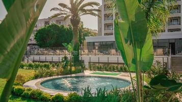 Una piscina circular rodeada de exuberante vegetación y palmeras, con un edificio moderno al fondo.
