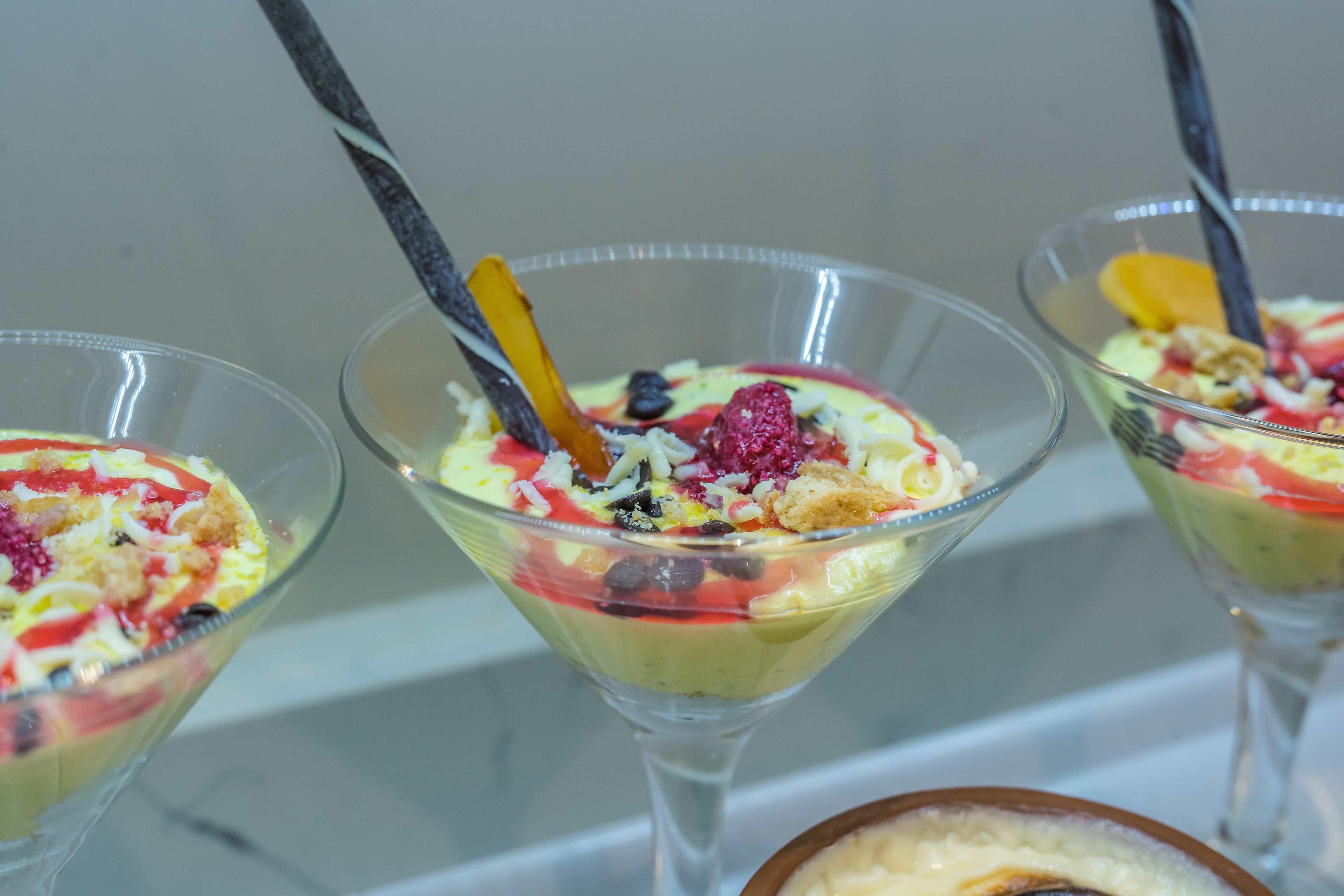 Three dessert glasses with fruit toppings and a spoon.