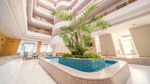 Un área de piscina interior moderna con un elemento central de agua, rodeada de asientos y plantas.