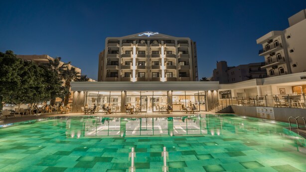 Un hotel con piscina, varios pisos y una entrada bien iluminada.