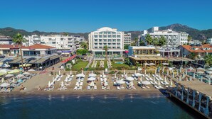 Un hotel frente al mar con varios pisos, un área de piscina central y una playa con tumbonas.