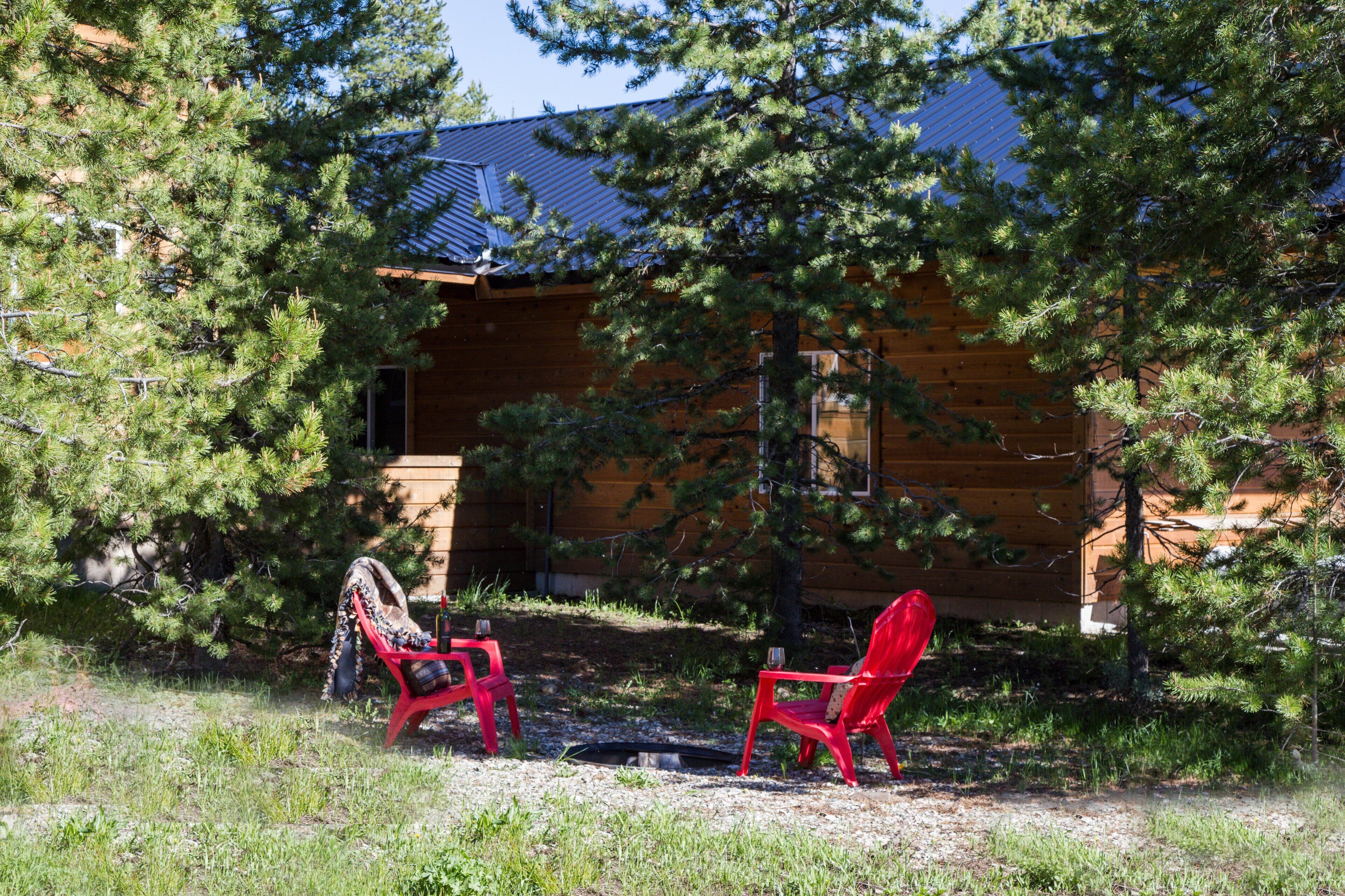 A cabin with two red chairs outside, surrounded by trees.