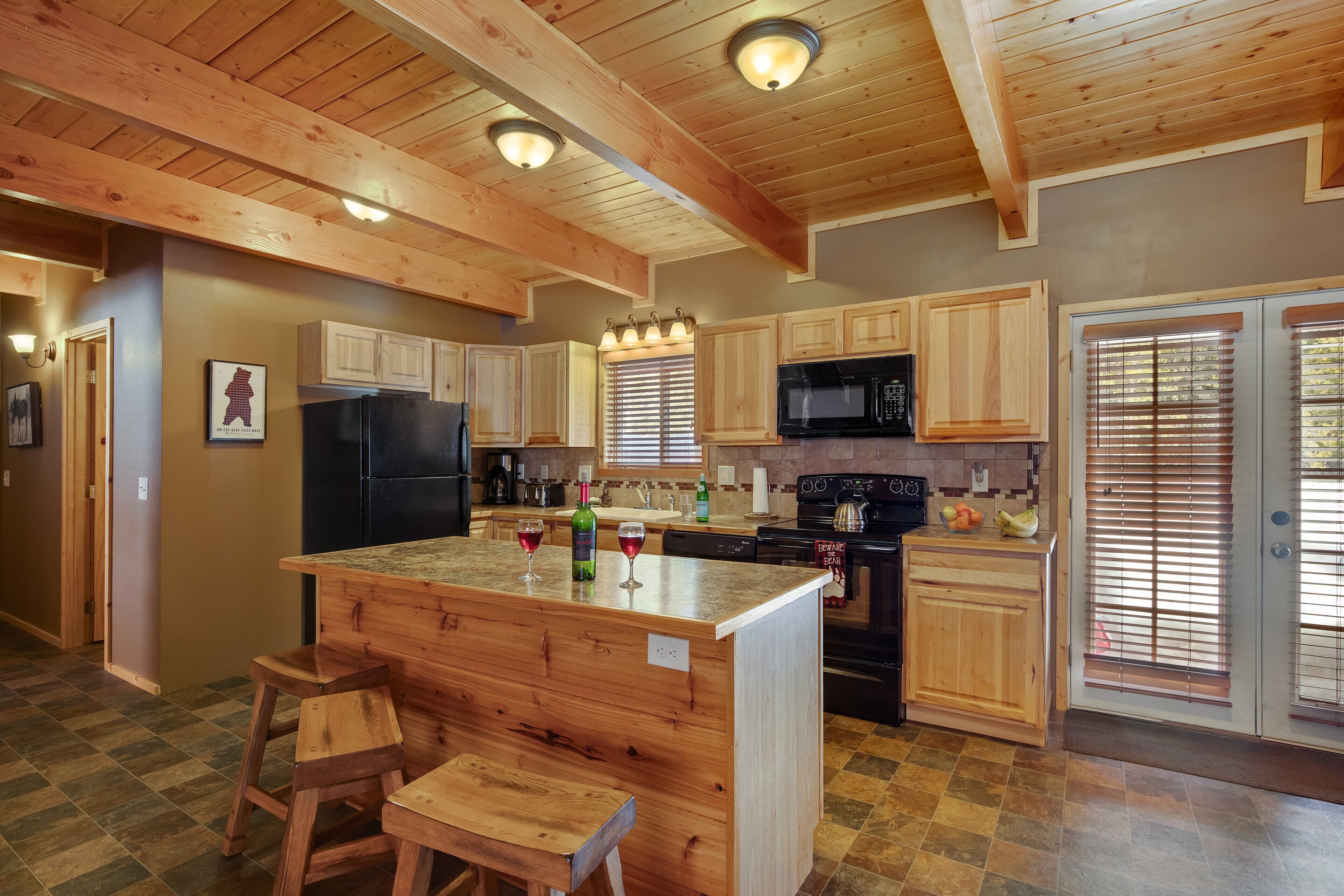 Una cocina con armarios de madera, una isla central con taburetes, un refrigerador, un microondas y una estufa.