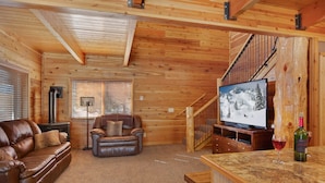 A cozy log cabin interior with a leather sofa, a recliner, a TV, and a wooden staircase. - Rimfire Refuge (Island Park)