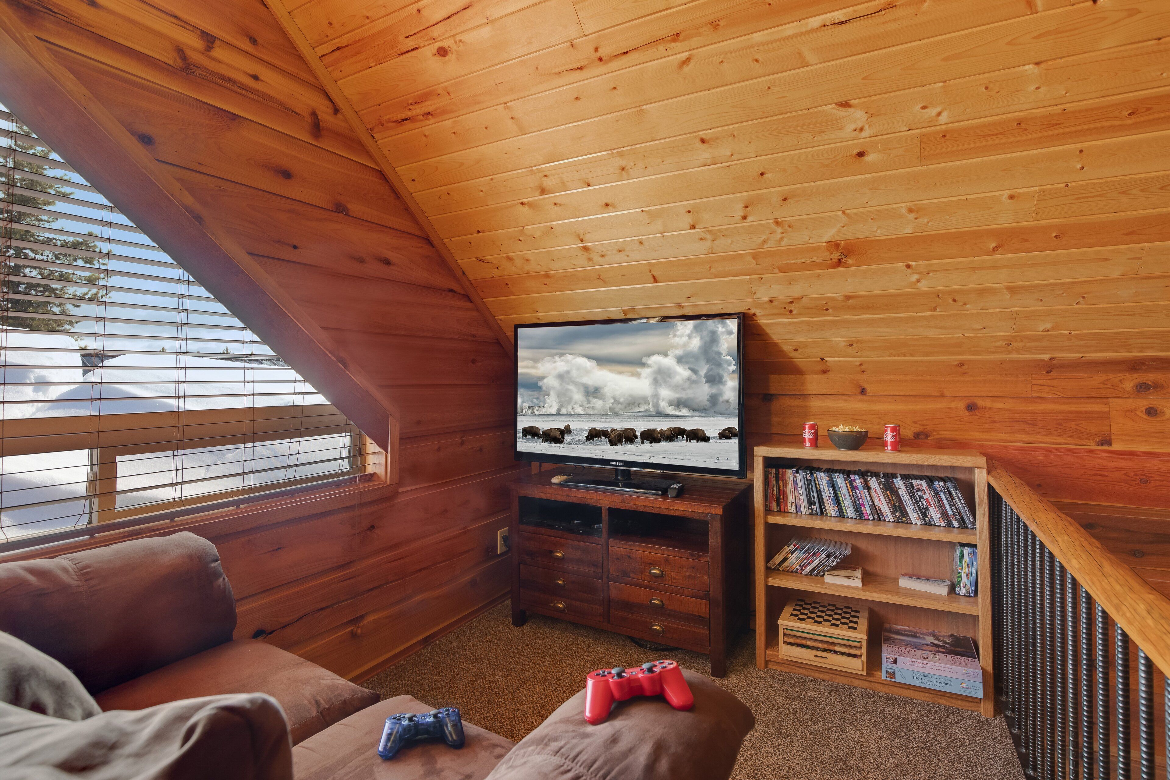 Ein gemütliches Zimmer mit Holzbalkendecke, einem Fernseher, einem Bücherregal und einem Sofa.