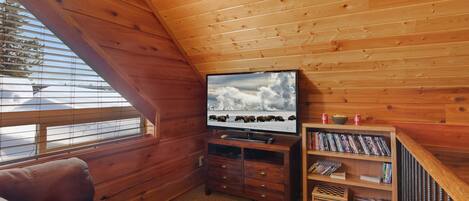 Ein gemütliches Zimmer mit Holzbalkendecke, einem Fernseher, einem Bücherregal und einem Sofa.