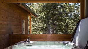 A hot tub in a wooden cabin with a view of trees. - Rimfire Refuge (Island Park)