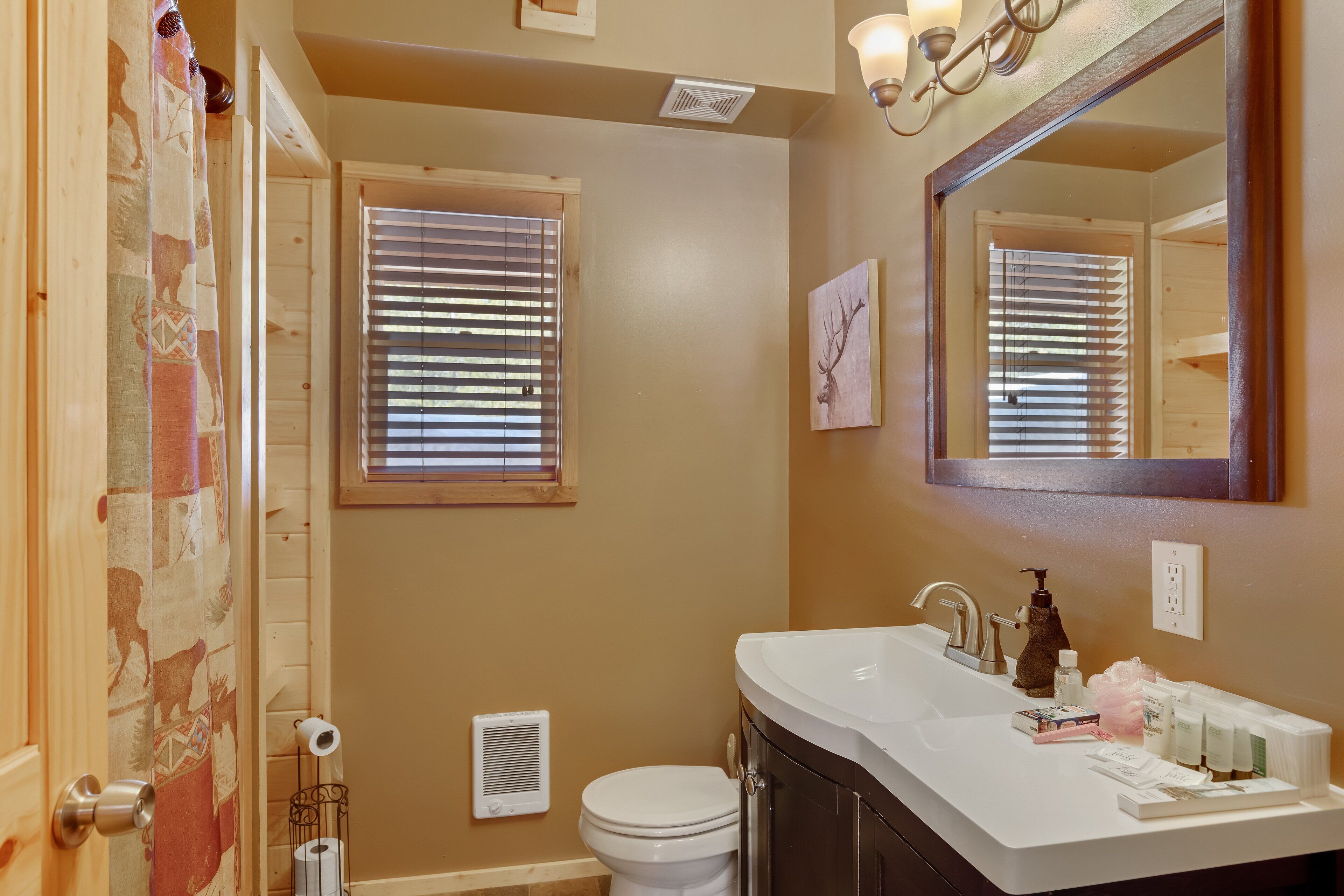Un baño con pared color crema, lavamanos blanco, espejo y retrete.