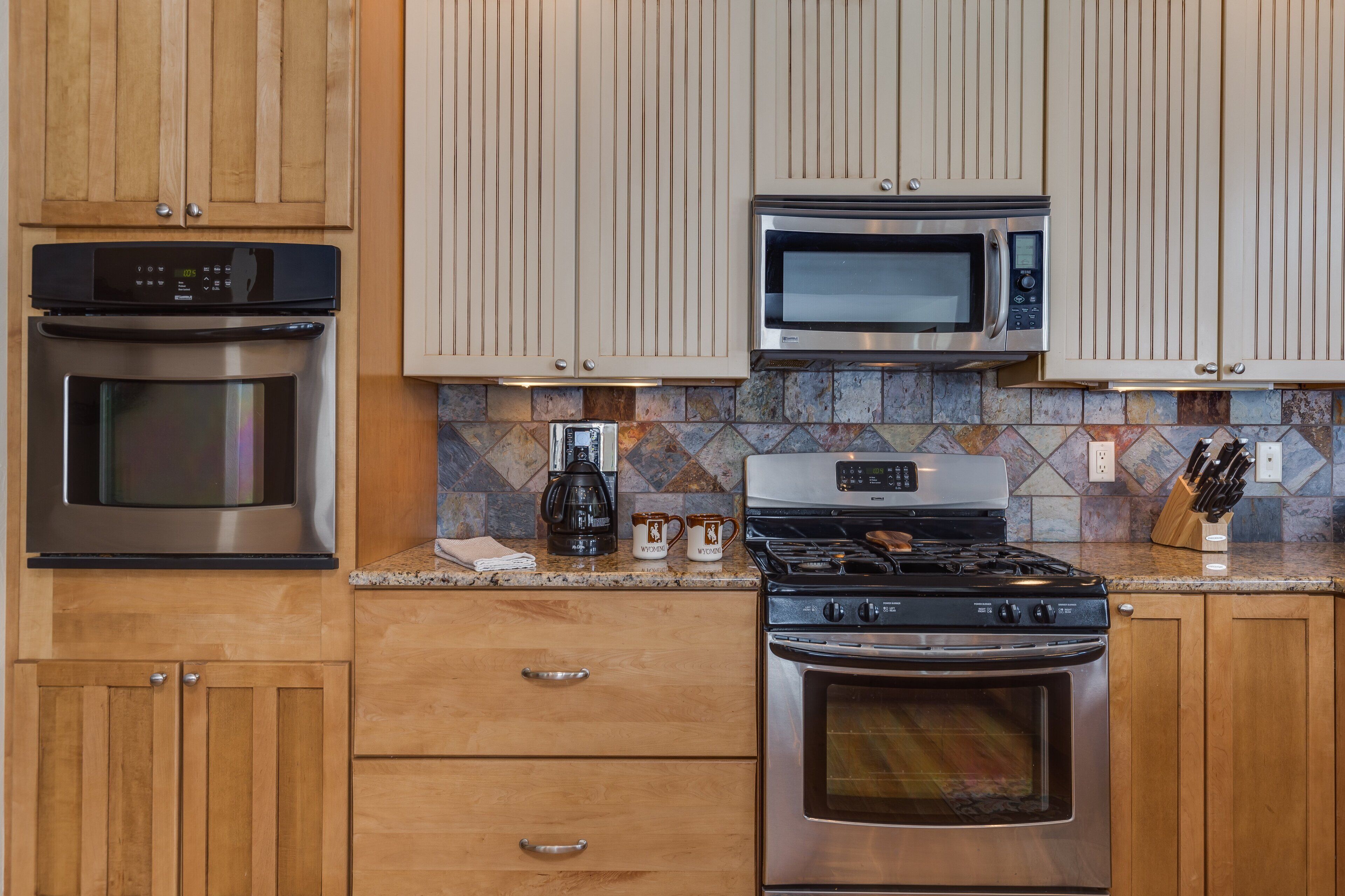 A kitchen with wooden cabinets, stainless steel appliances including an oven, microwave, and stove, and a tiled backsplash.