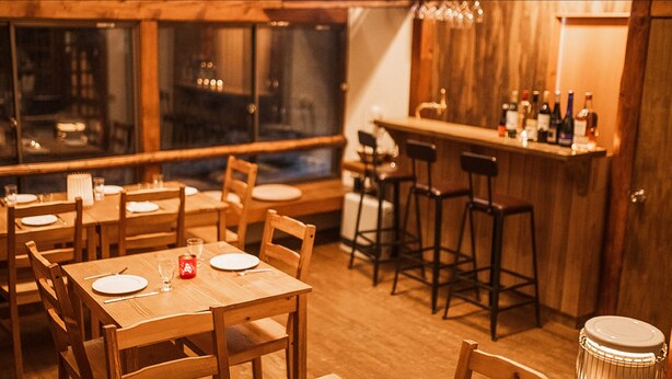 Un restaurante con mesas y sillas de madera, una zona de bar con taburetes y un tambor en primer plano.