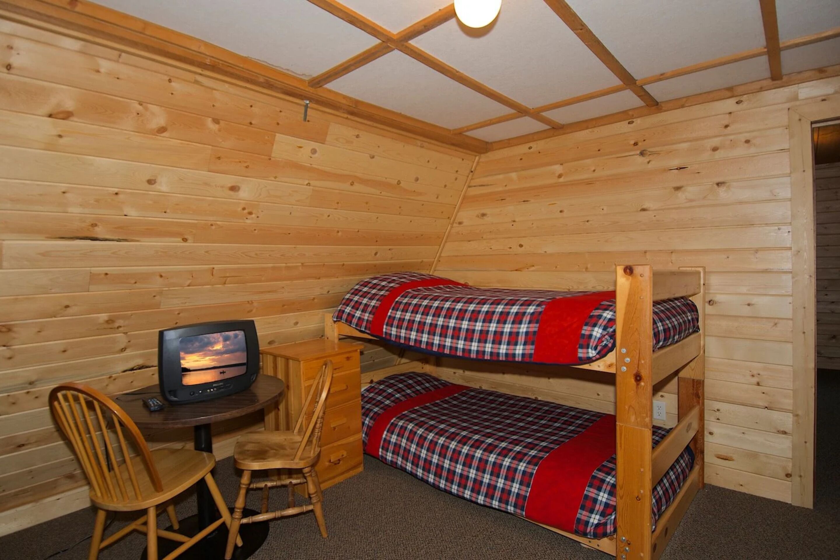 Une chambre dans un chalet en bois, avec des lits superposés, un petit bureau et un téléviseur.