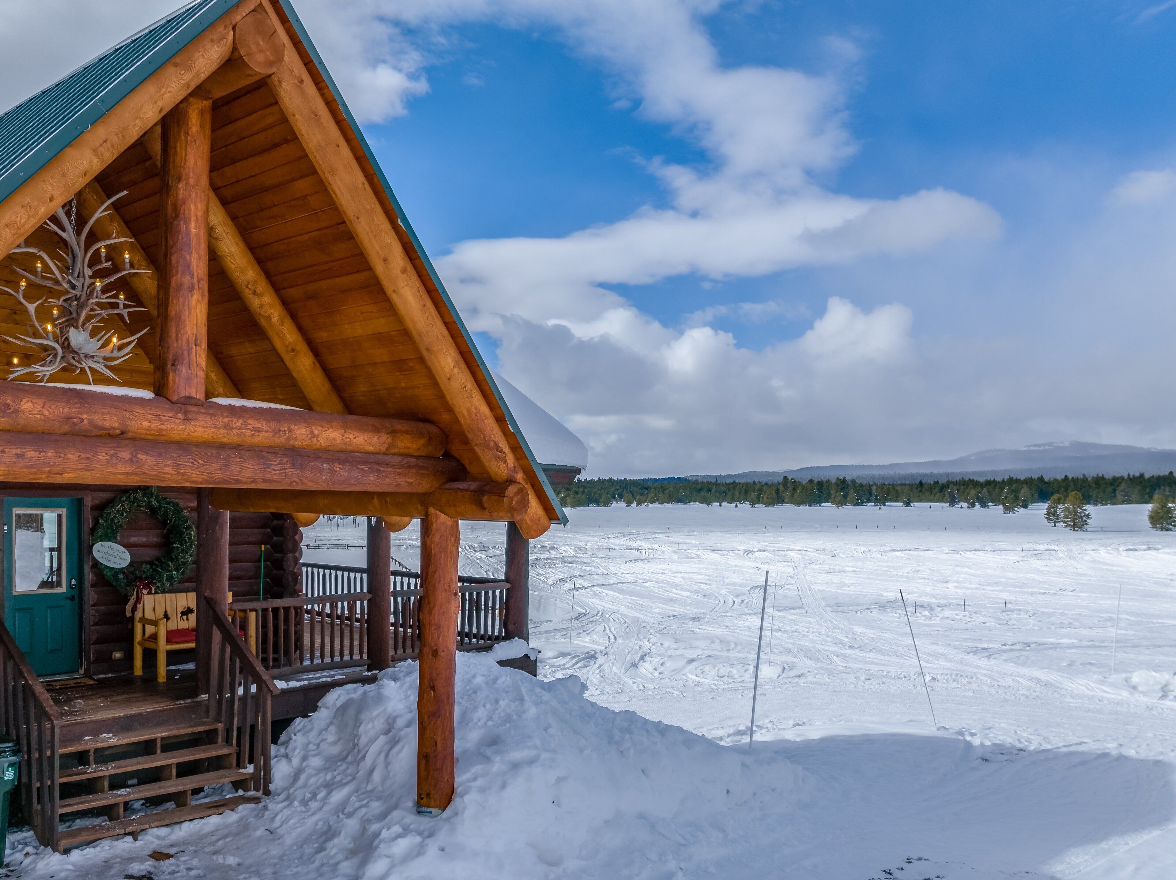 Uma cabana de tronco com varanda, grinalda e paisagem coberta de neve.