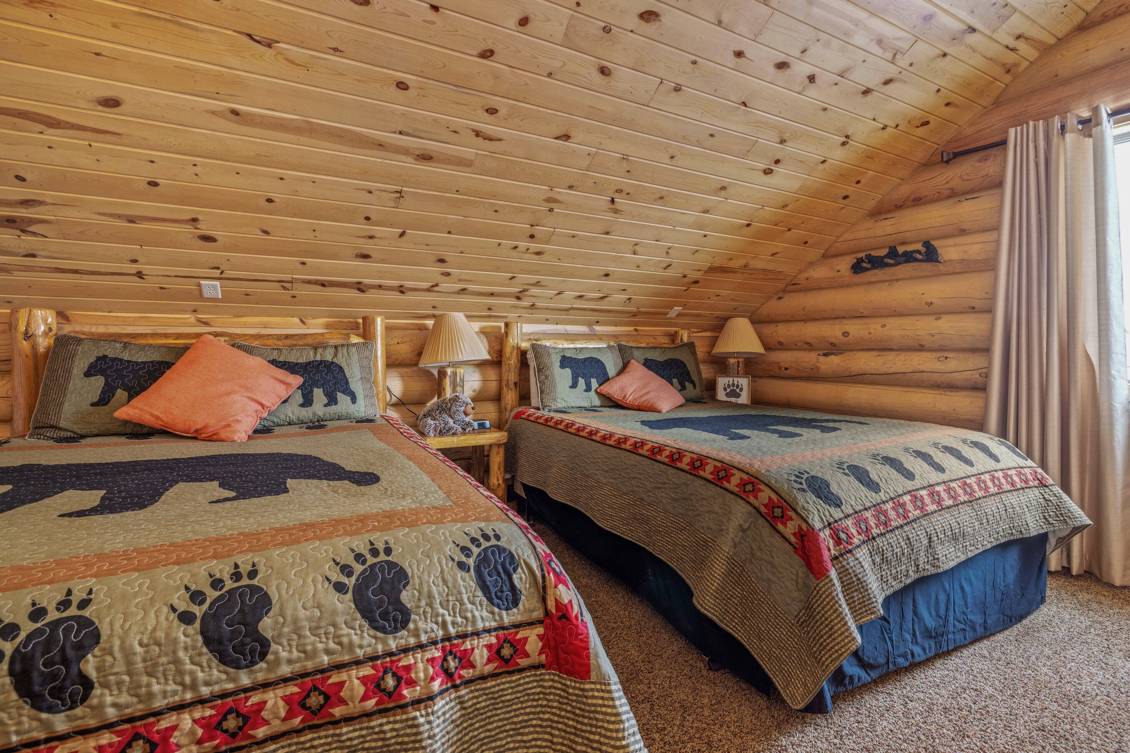 Une chambre confortable dans un chalet, avec deux lits, chacun orné d’une courtepointe au motif unique, des murs en bois et une fenêtre avec des rideaux.