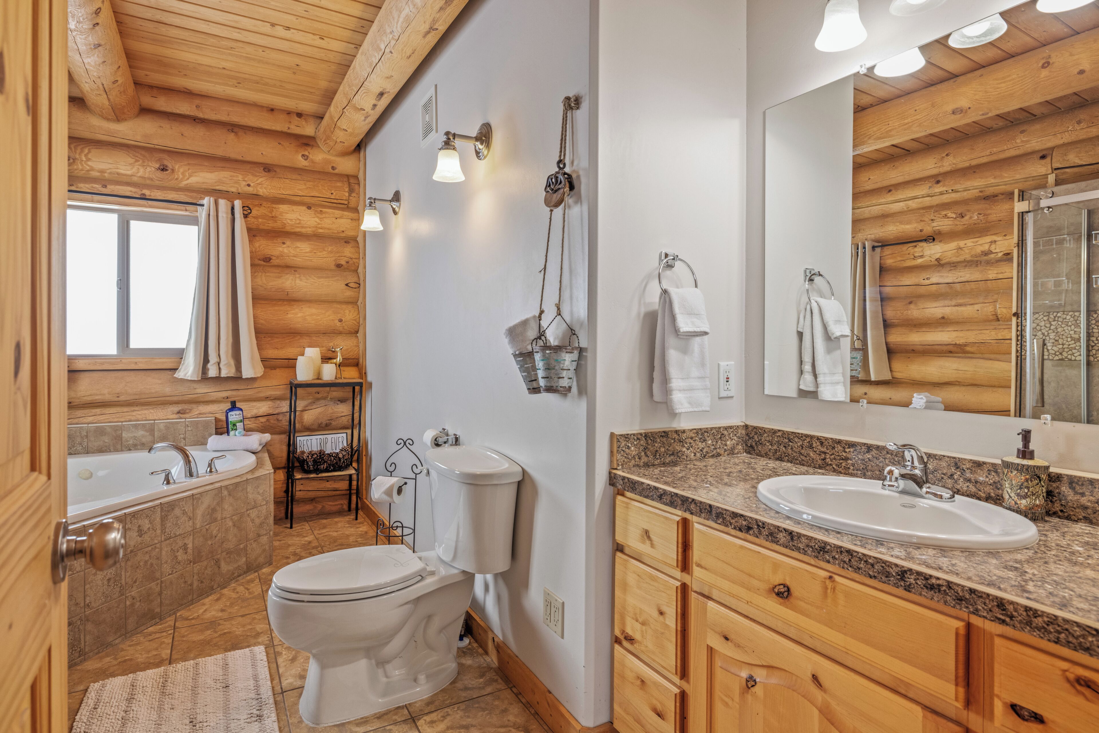 A wooden cabin bathroom with a bathtub, toilet, sink, and a large mirror.