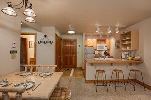 Una cocina con armarios de madera, microondas y un lavabo. Hay taburetes y una mesa de comedor con platos y cubiertos.