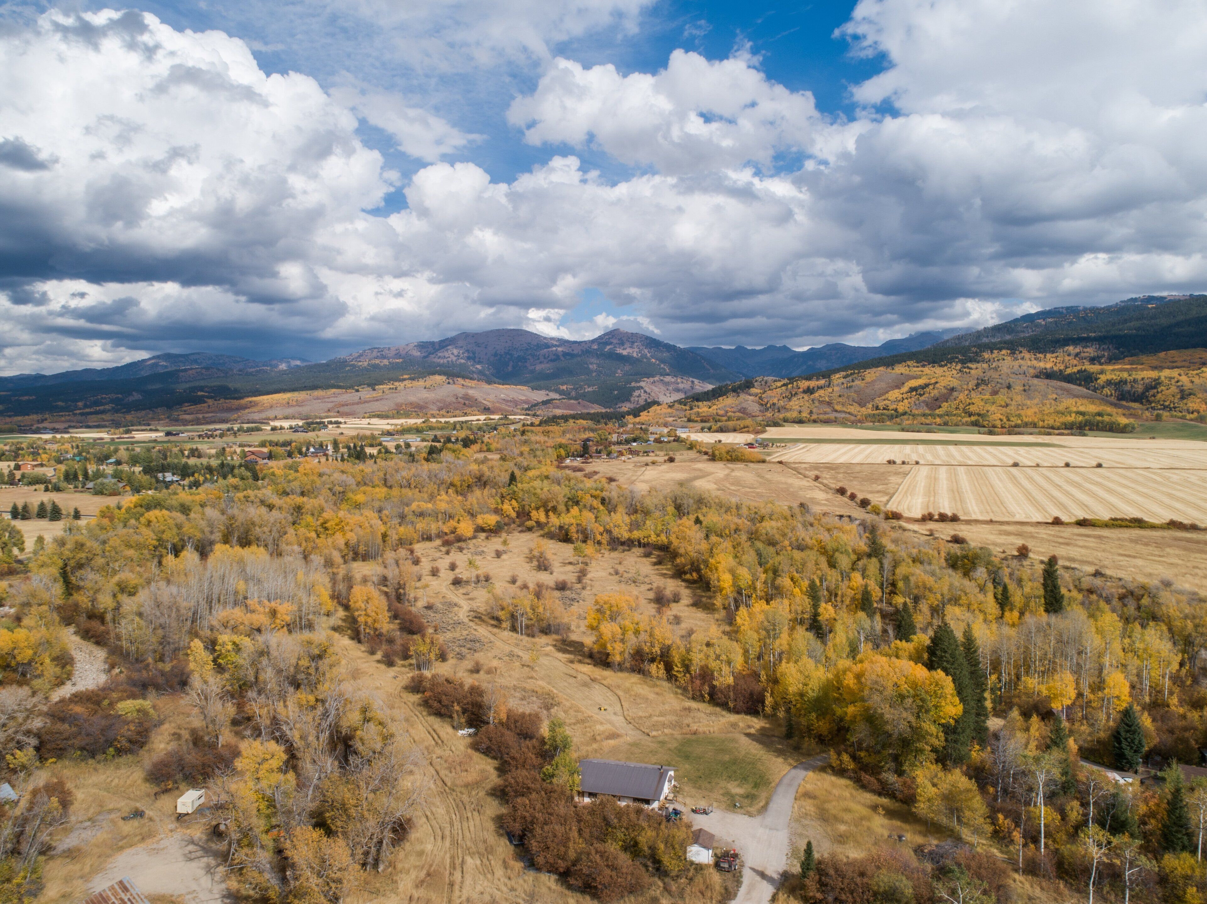 An aerial view of a rural landscape with fields, trees, and mountains in the background.