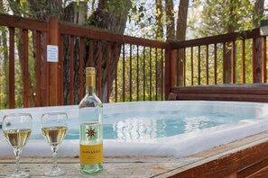 Eine Holzterrasse mit Whirlpool, zwei Weingläsern und einer Flasche Mirassou Wein.