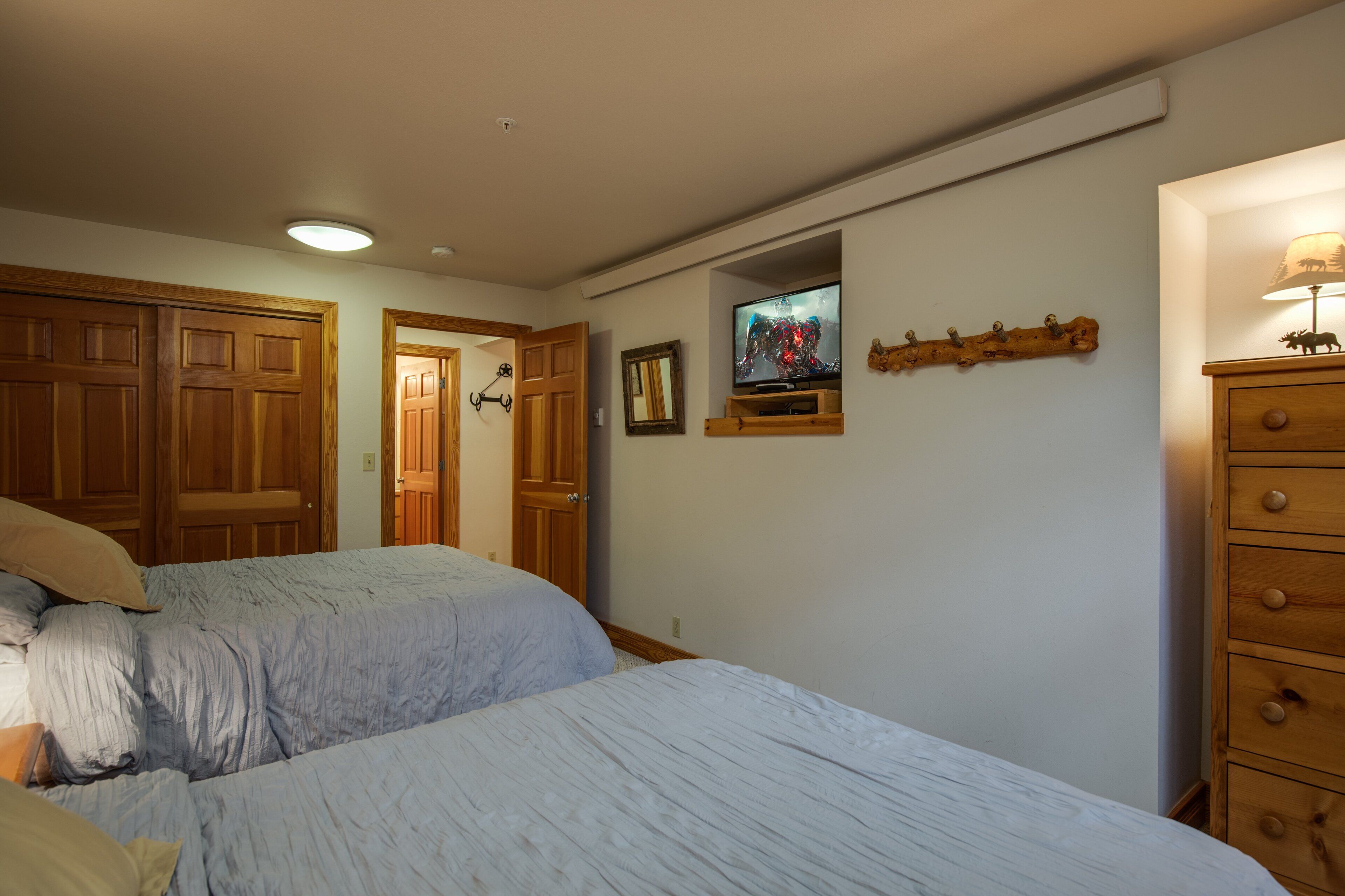 A bedroom with two beds, wooden wardrobes, a television, and a dresser.