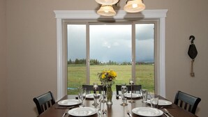 A dining table set for six with a vase of flowers, set against a large window overlooking a grassy field. - Teton Harmony (Driggs)