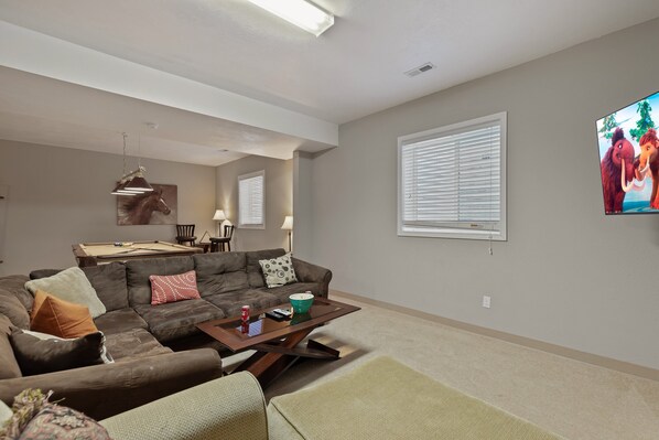 A living room with a sectional sofa, a coffee table, and a television mounted on the wall. - Teton Harmony (Driggs)